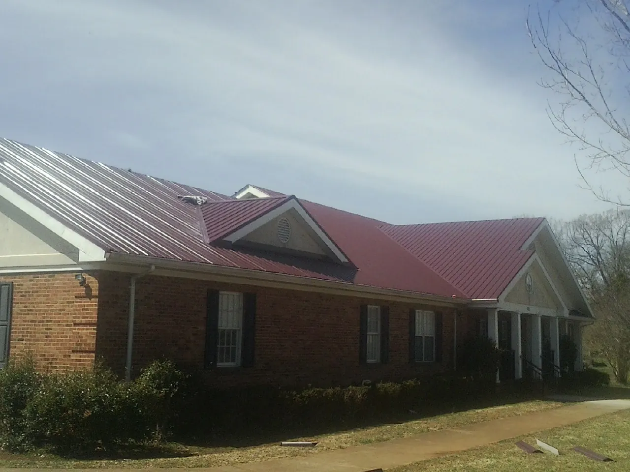 Red metal roof with gabled entries on a long brick building, from a Hail Damage Roof Repair job in Ixonia