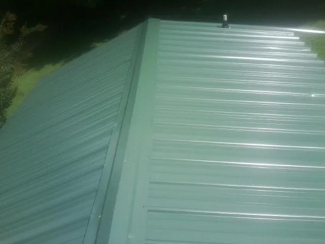 New green metal panels meeting at the ridge of a roof — Flat Roof Repair work by our crew in Ixonia