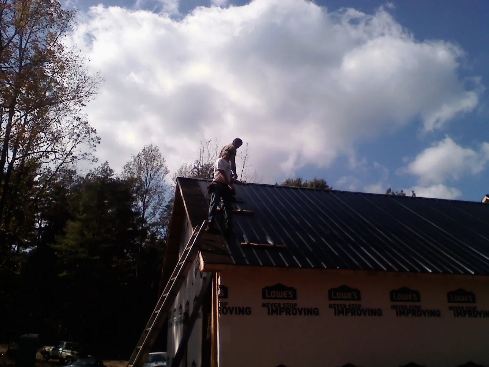 Roofer fastening dark metal panels high against a cloudy sky, from a Roof Inspection job in Ixonia
