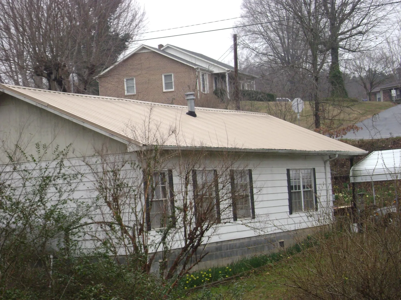Tan metal roof on a white sided house set into a hillside — Commercial Roofing by Roofing Brothers in Ixonia